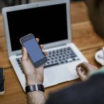 Pessoa com notebook segurando um celular