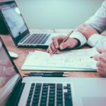 Homens escrevendo em um papel com notebooks do lado de cada um