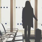 Mulher com uma mala de frente a uma porta