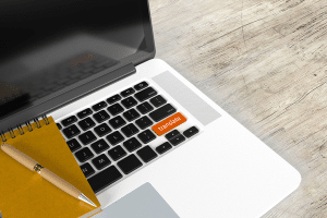 Imagem de um laptop com uma tecla em laranja escrito translate, ao lado ainda em cima do laptop tem um pequeno caderno e caneta